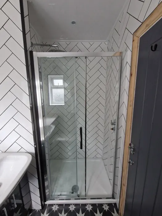 Shower enclosure with white herringbone tiles and a black frame