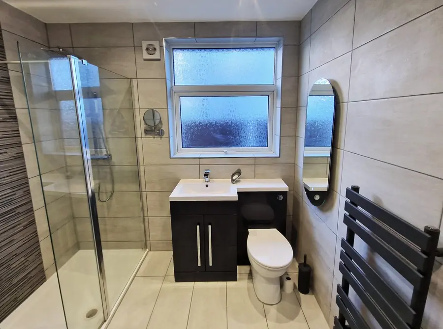 Grey tiled bathroom with walk-in shower and black towel radiator
