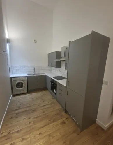 Rental flat kitchen with grey units and a tall fridge freezer
