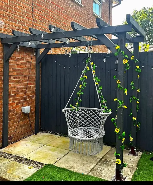 Black-painted pergola with a hanging chair and climbing plants